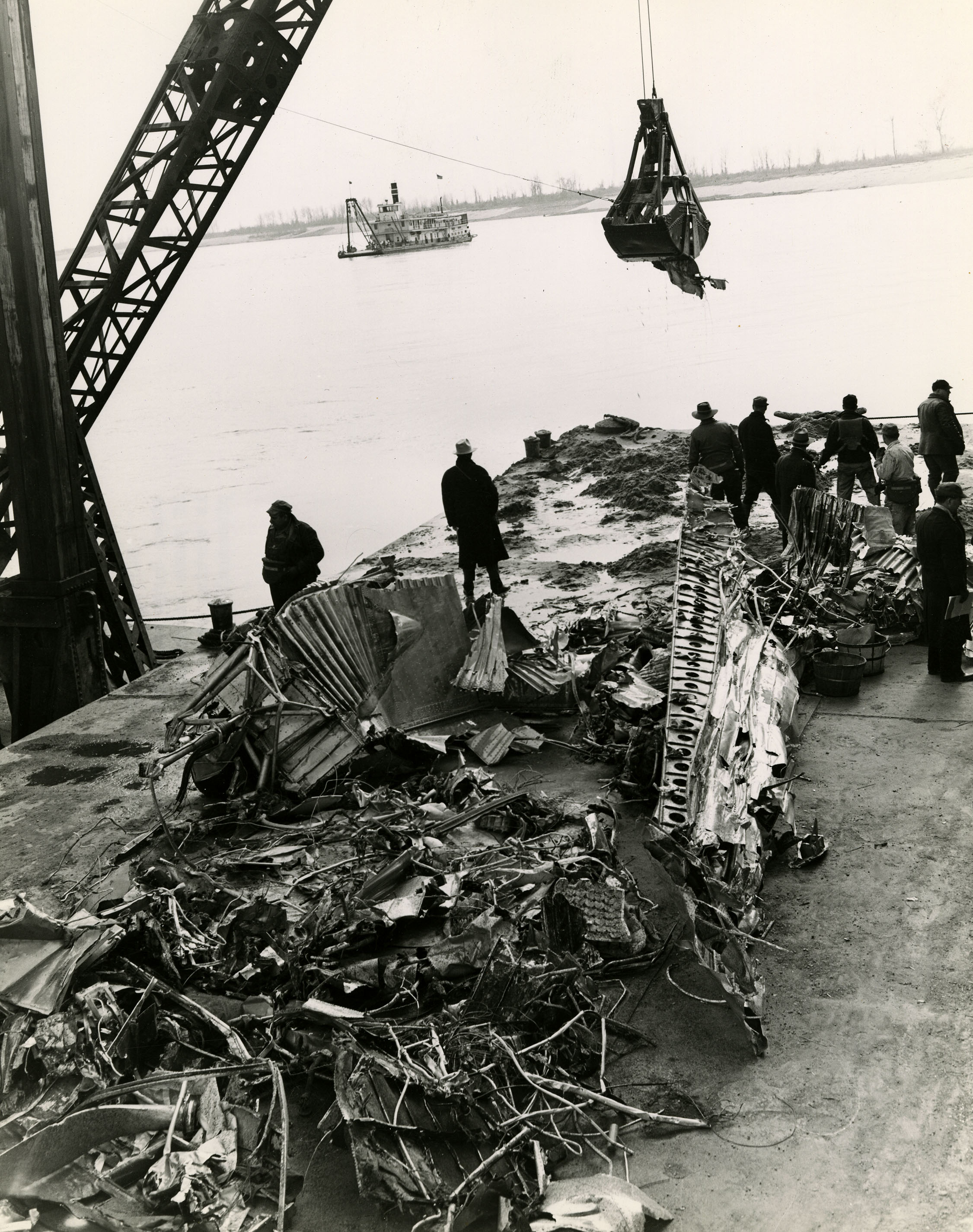 a shovel on a crane about to unload debris onto a pile of other metal parts